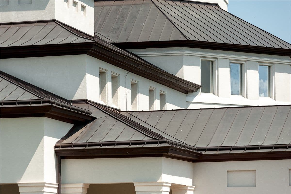 Modern house with multiple sloped brown roofs and white stucco walls. Several small windows line the second floor, creating a clean, geometric design.